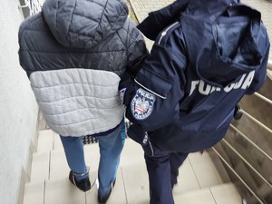 Na zdjęciu policjantka prowadzi zatrzymanego mężczyznę po schodach.