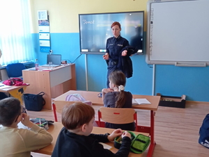 Na zdjęciu policjantka prowadzi prelekcje dla dzieci, które znajdują się w sali.