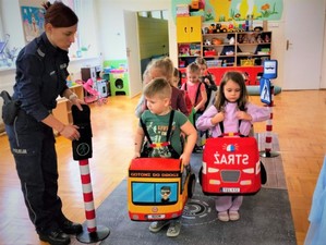 Na zdjęciu policjantka uczy grupę dzieci przepisów ruchu drogowego wykorzystując mobilne miasteczko ruchu drogowego.