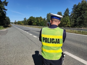 Na zdjęciu policjant ruchu drogowego stoi przy drodze z ręcznym miernikiem prędkości.