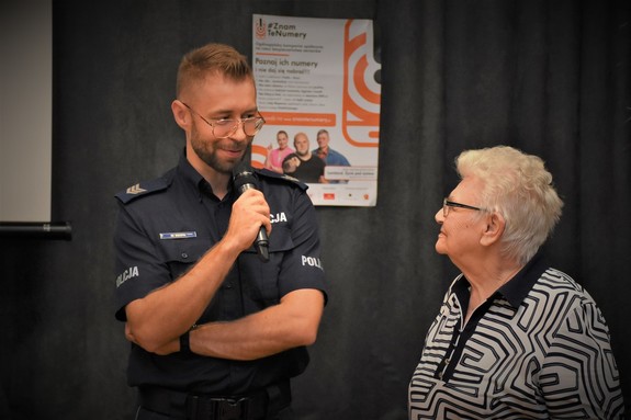Na zdjęciu umundurowany policjant rozmawia ze starszą kobietą.