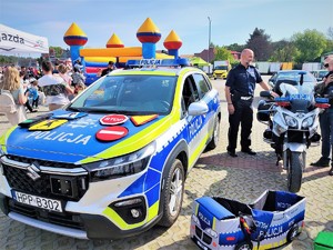 Zdjęcie, na którym jest umundurowany policjant obok radiowozu i motocykla policyjnego.