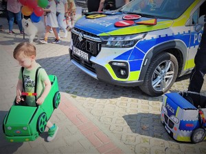 Na zdjęciu chłopczyk ma na sobie autochodzik przy radiowozie policyjnym.