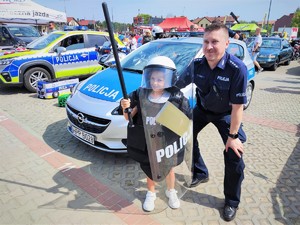 Na zdjęciu umundurowany policjant stoi z dziewczynką, która przebrała się za policjanta.