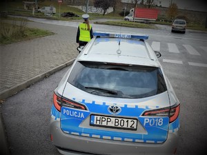 Na zdjęciu policjantka stoi przy radiowozie, który znajduje się przy przejściu dla pieszych.