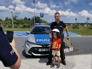 Na zdjęciu policjant z dzieckiem, które ma założone elementy policyjnego wyposażenia.