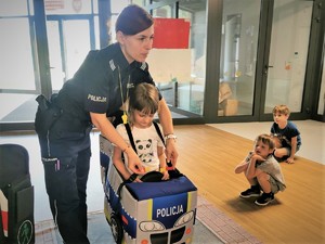 Na zdjęciu policjantka zakłada dziecku autochodzik do zabawy i nauki przepisów.