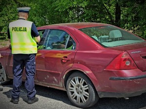 Na zdjęciu policjant stoi przy samochodzie.