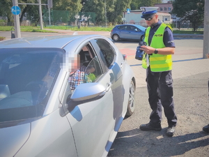 Na zdjęciu policjant stoi przy samochodzie z miernikiem prędkości .