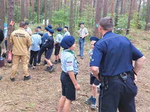 Na zdjęciu policjant rozmawiający z harcerzami w lesie.