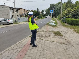 Na zdjęciu policjantka przy drodze mierzy prędkość.