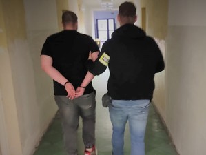 Na zdjęciu policjant prowadzi zatrzymanego mężczyznę przez korytarz.