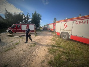 Na zdjęciu wozy strażackie oraz idący policjant.