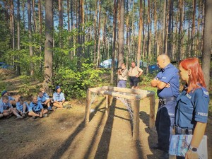 Na zdjęciu policjant i policjantka przemawiają do grupy harcerzy.