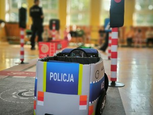 Na zdjęciu z przodu pojazd autochodzika z napisem policja, w oddali widoczne policjantki i dzieci.