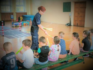 Na zdjęciu policjantka rozdaje odblaski dzieciom na sali gimnastycznej.