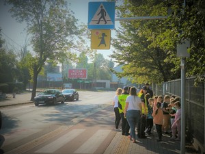 Na zdjęciu grupa dzieci z policjantkami i wychowawcą przy oznakowanym przejściu dla pieszych.