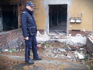 Na zdjęciu policjant stojący przed opuszczonym budynkiem