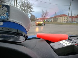 Zdjęcie przedstawiające czapkę policyjną i alkomat na podszybiu oraz kontrolującego trzeźwość policjanta.