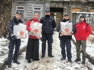 Na zdjęciu policjanci oraz przedstawiciele Caritas z paczkami na dworze.