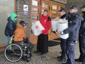 Na zdjęciu ksiądz z policjantami przekazuje paczkę potrzebującym.