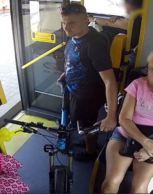 Na zdjęciu mężczyzna w autobusie stoi przy niebieskim rowerze.