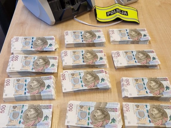 Na zdjęciu pieniądze ułożone na stole, opaska z napisem POLICJA i liczarka banknotów.