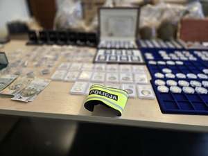 Na zdjęciu opaska odblaskowa z napisem POLICJA i zabezpieczone przez policjantów rzeczy na stole w postaci pieniędzy i srebra.