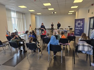 Zdjęcie grupowe, dzieci podnoszą ręce by zadać policjantce pytanie.