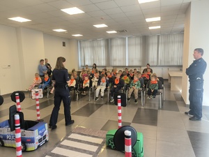 Na zdjęciu policjantka i policjant prowadzą prelekcje dla grupy dzieci.