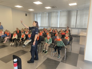 Na zdjęciu policjantka trzymająca szklankę przed grupą dzieci.