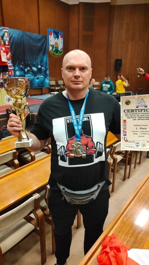 Na zdjęciu mężczyzna trzyma w rękach dyplom i puchar za zajęcie 1 miejsca.