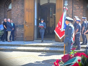 Na zdjęciu policjant wychodzi z kościoła i niesie na poduszce czapkę policyjną.