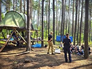 Na zdjęciu widzimy policjantkę i strażaka, którzy rozmawiają z uczestniczkami obozu.