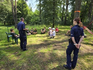 Na zdjęciu widzimy policjantkę i policjanta, którzy rozmawiają z uczestniczkami półkolonii jeździeckich.