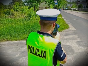 NA zdjęciu policjant z radarem prędkości przy drodze.