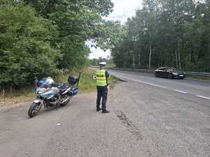 Na zdjęciu policjant drogówki stojący przy motocyklu policyjnym i drodze.