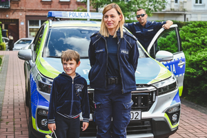 Na zdjęciu policjantka i policjant stoją z chłopcem przy radiowozie.