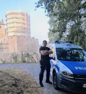 Na zdjęciu policjant stojący przy radiowozie.