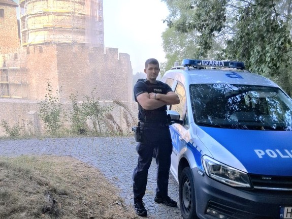 Na zdjęciu policjant stojący przy radiowozie.