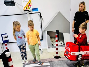Na zdjęciu grupa dzieci korzysta z mobilnego miasteczka drogowego przy udziale policjantki.