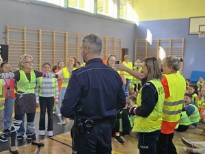 Na zdjęciu policjantka i policjant wraz z innymi uczestnikami mody odblaskowej na sali gimnastycznej podczas konkursu.