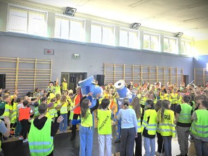 Na zdjęciu grupa dzieci i uczniów machają odblaskami na sali gimnastycznej.