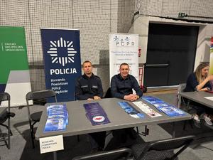 Na zdjęciu umundurowany i nieumundurowany policjant na stanowisku profilaktycznym podczas Dnia Seniora.