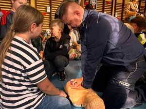 Na zdjęciu dziewczyna i umundurowany policjant podczas resuscytacji prowadzonej na manekinie.