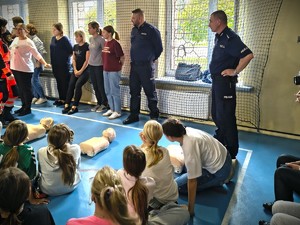 Na zdjęciu policjanci z uczniami na sali gimnastycznej podczas resuscytacji krążeniowo oddechowej ćwiczonej na manekinach.