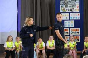 Na zdjęciu policjantka pokazuje odblaskowy napis policja na mundurze policjanta.