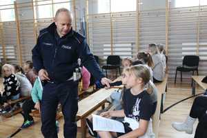 Na zdjęciu policjant z mikrofonem zadaje pytanie uczennicy na sali gimnastycznej.