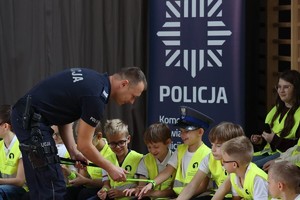 Na zdjęciu umundurowany policjant rozdaje dzieciom odblaski.