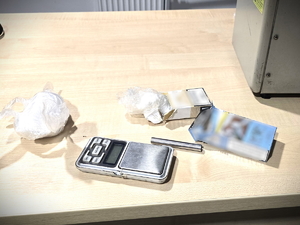 Na zdjęciu znajdują się dwie paczki po papierosach, biała zbrylona substancja w worku i waga elektroniczna.